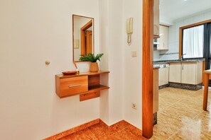 Un passadís que condueix a una cuina amb un armari de fusta, un mirall, una planta i un telèfon a la paret.