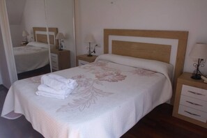 A neatly made bed with a floral bedspread, a bedside table with a lamp, and a mirror on the wall.
