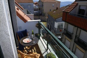 En balkon med et bord dækket til to, en stol, en potteplante og udsigt til omkringliggende bygninger.