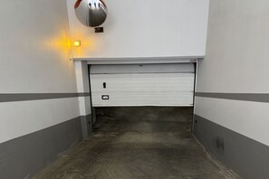 Autotallin sisäänkäynti, jossa on kiinni oleva autotallin ovi, turvakamera ja seinässä oleva valaisin.