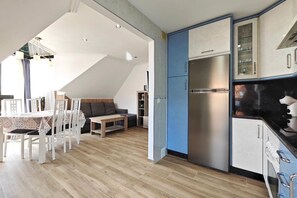 A modern kitchen with a stainless steel refrigerator, a dining area with a table and chairs, and a living space with a sofa and a coffee table.