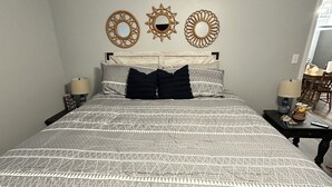 Ein Schlafzimmer mit einem Bett, zwei Nachttischen, einem Wandspiegel und einem Fenster.