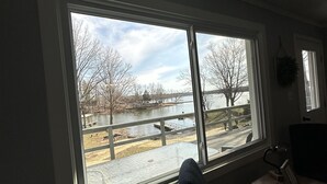 Ein Zimmer mit großem Fenster mit Blick auf einen Fluss und eine Brücke. Ein Schreibtisch mit Computer und Stuhl sind vorhanden.