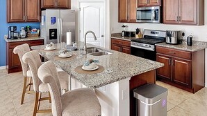 A kitchen with granite countertops, wooden cabinets, a stainless steel refrigerator, a microwave, and a stove.