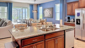 A modern kitchen with granite countertops, wooden cabinets, a stainless steel refrigerator, and a dining area with a view.
