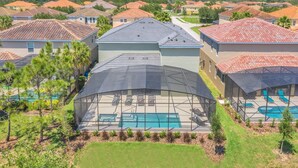 A residential area with a large house featuring a covered outdoor pool area with lounge chairs.