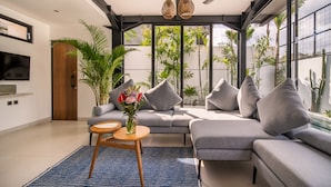 A modern living room with a grey sofa, a small wooden table, and a blue rug. There is a TV mounted on the wall and a ceiling fan. - Private Pool • Daily Housekeeping • Walk to Canggu (Canggu)