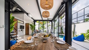 A dining area with a wooden table set for a meal, surrounded by large windows and a view of the outdoors. - Private Pool • Daily Housekeeping • Walk to Canggu (Canggu)