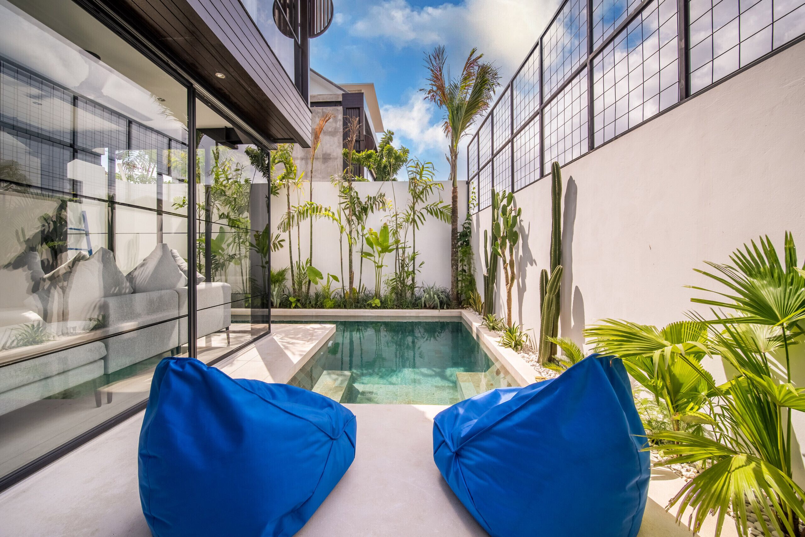 A modern outdoor pool area with blue cushioned seating and lush tropical plants.