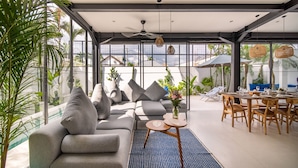 A modern living room with a grey sofa, a round coffee table, and a dining area with wooden chairs and a table. - Private Pool • Daily Housekeeping • Walk to Canggu (Canggu)