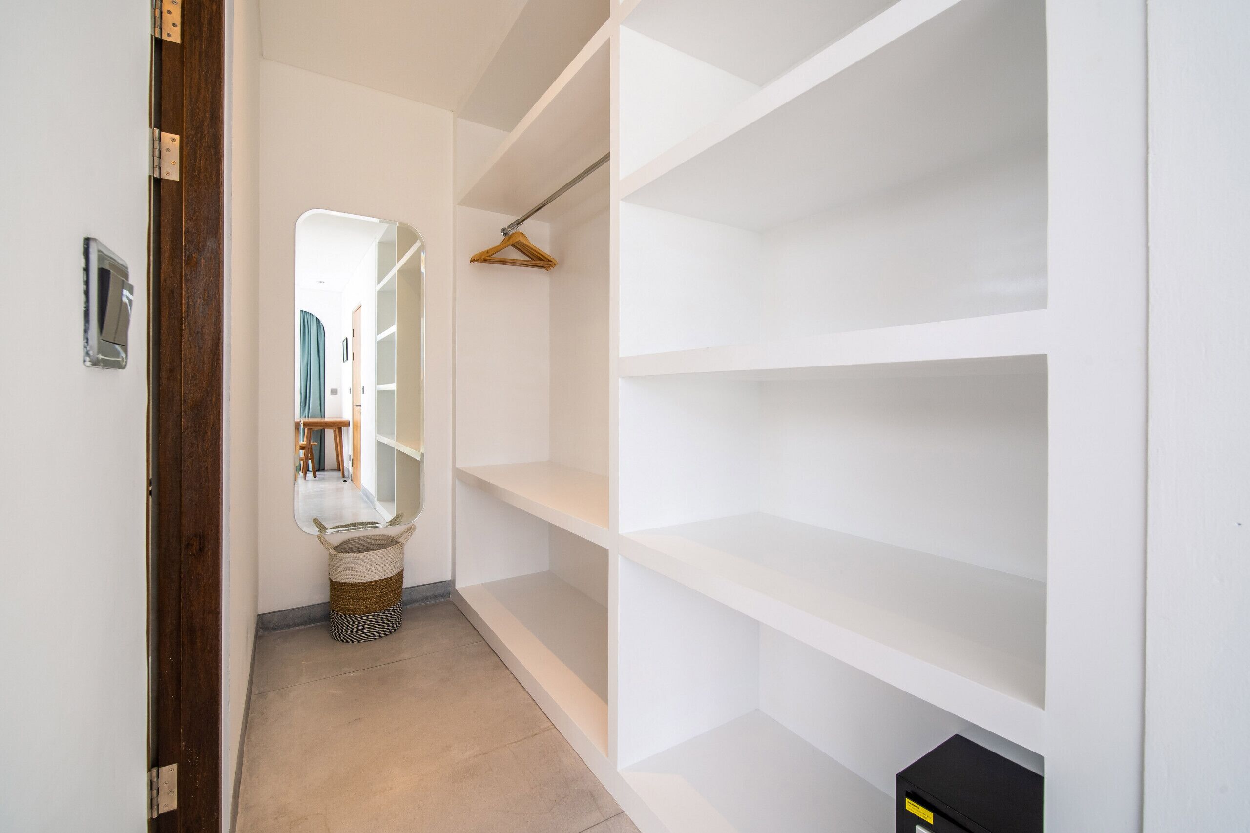 A hallway with a wooden door, a mirror, and a white closet with empty shelves.