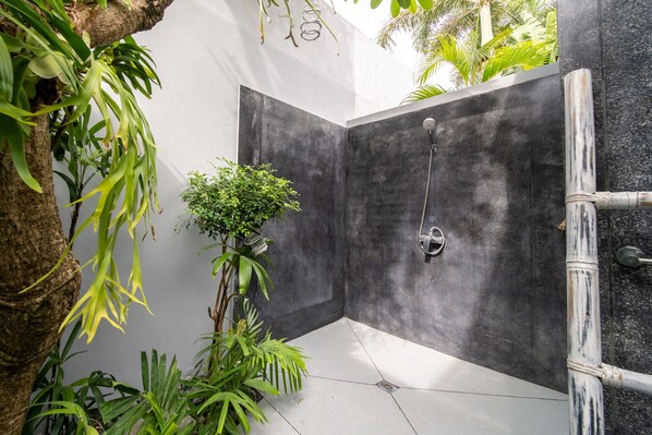 A modern shower area with a dark wall, a showerhead, and surrounding greenery.