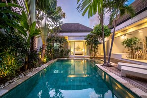 Una piscina circondata da piante tropicali, con un edificio sullo sfondo.