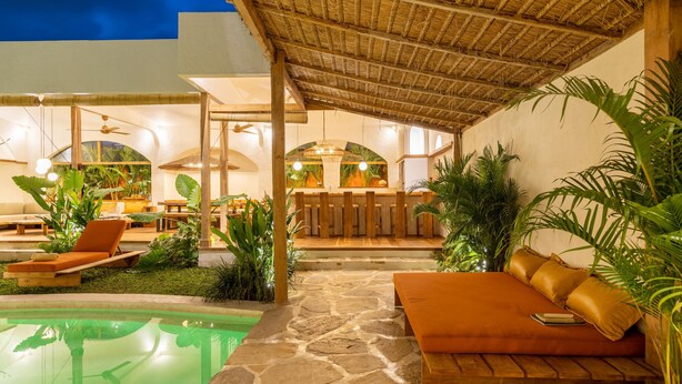 A pool area with lounge chairs and a stone pathway leading to a seating area with cushions. - Tropical Garden | Three Bedrooms | Walk to Cafés (Kerobokan)