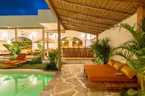A pool area with lounge chairs and a stone pathway leading to a seating area with cushions.
