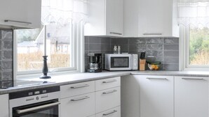 Eine Küche mit weißen Schränken, einer Mikrowelle, einer Kaffeemaschine und einem Fenster mit Vorhängen.