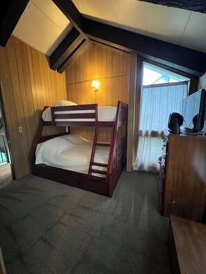 Een stapelbed met houten frame en witte beddengoed, een bureau met stoel, en een raam met gordijnen.
