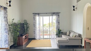 Un salon moderne avec un comptoir noir, un canapé, un téléviseur et une grande fenêtre avec des rideaux.