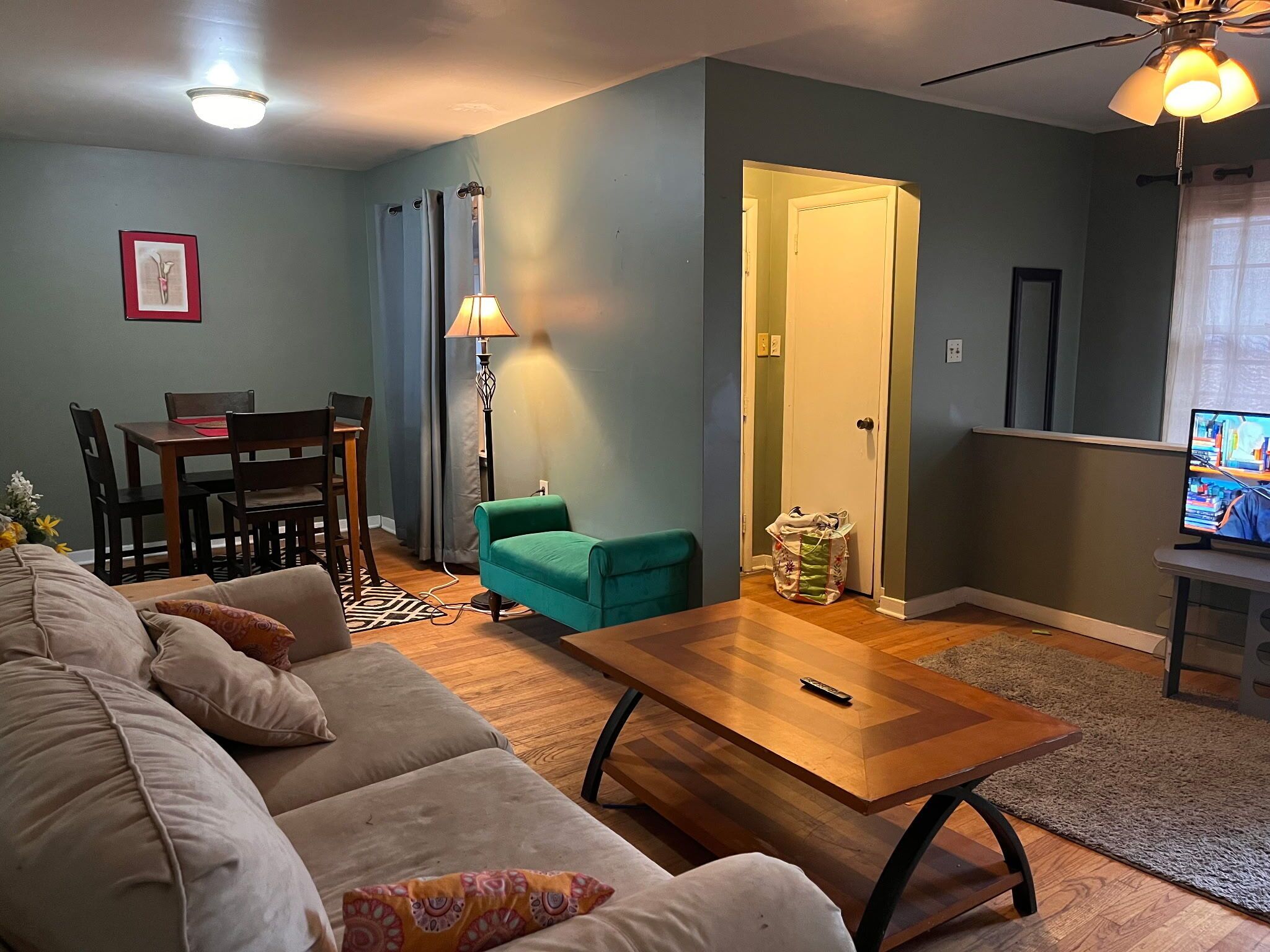 A living room with a sofa, a wooden coffee table, a lamp, a television, and a door leading to another room.