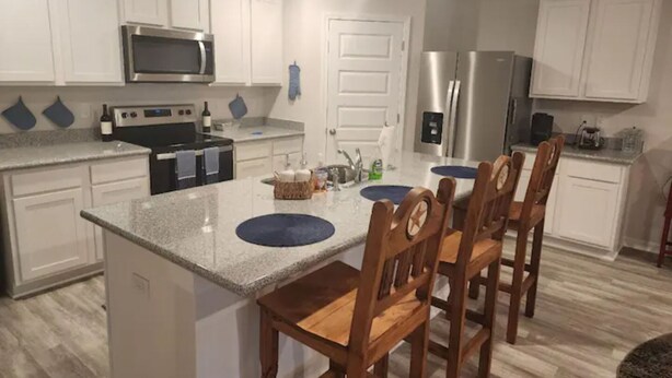 A modern kitchen with white cabinets, stainless steel appliances, and a central island with chairs. - Casa De los Pensacola (Pensacola)