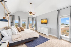 A bedroom with a bed, a ceiling fan, a TV, a dresser, and a view of the outside. - Canal | Hot Tub | Large Deck | Private Dock | Pets (Galveston)