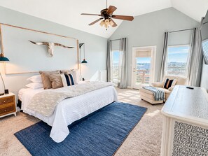 A bedroom with a bed, bedside tables, a ceiling fan, a large window with curtains, and a view of the outdoors. - Canal | Hot Tub | Large Deck | Private Dock | Pets (Galveston)