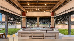 Un bain à remous installé sous une structure en bois, avec vue sur une étendue d’eau et des bâtiments en arrière-plan.