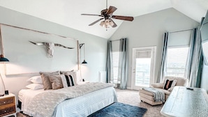 Une chambre à coucher comprenant un lit, des tables de chevet, un ventilateur de plafond et une grande fenêtre avec des rideaux.
