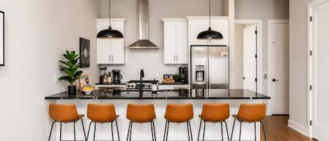 A modern kitchen with a central island, bar stools, pendant lighting, and stainless steel appliances.