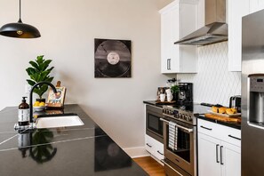 Een moderne keuken met een zwart aanrecht, roestvrijstalen apparatuur en een hangende pendelverlichting.