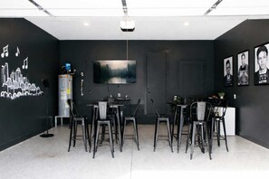 A modern room with a flat-screen TV, a cityscape mural, and a dining area with chairs and tables.