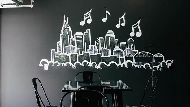 A conference room with a black table and chairs, a city skyline mural with musical notes, and a projector mounted on the ceiling. - Nashville Getaway • Hot Tub & Sleeps 12 (Nashville)