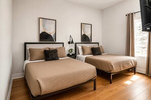 Een hotelkamer met twee bedden, een nachtkastje, een lamp en kunst aan de muur.