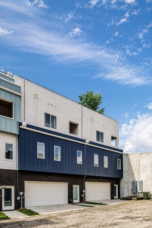 A multi-story residential building with a garage, a visible tree, and a clear sky.