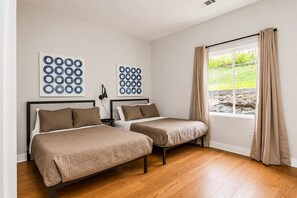 Une chambre avec deux lits, une fenêtre avec des rideaux et des œuvres d’art accrochées au mur.