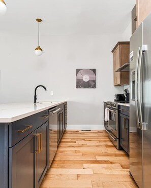 A modern kitchen with a central island, stainless steel appliances, and a wooden floor. - Nashville Retreat • Rooftop Skyline & 12 Guests (Nashville)