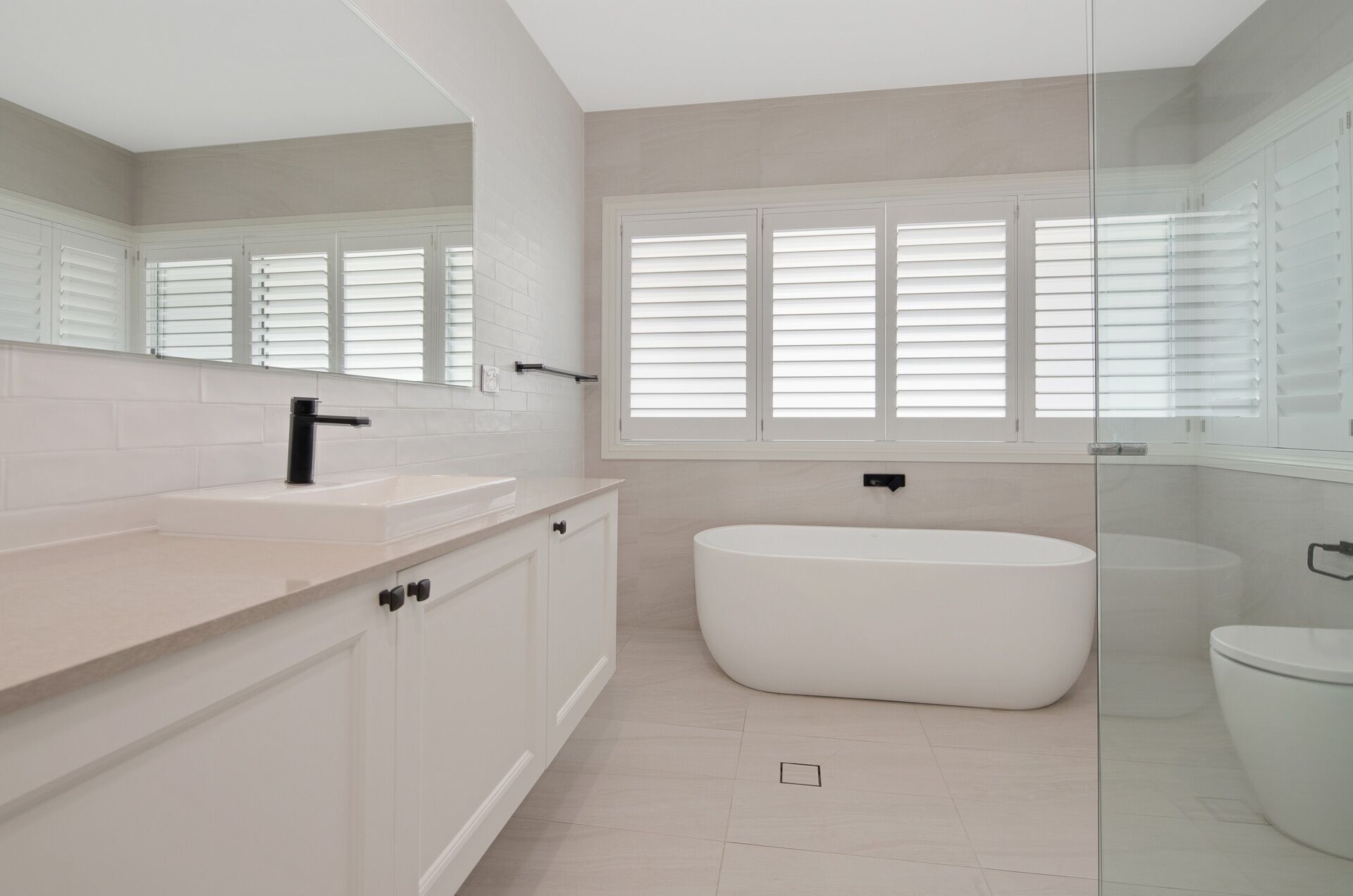 Une salle de bain moderne avec une baignoire sur pieds, un grand miroir et une fenêtre équipée de stores.