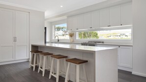 Une cuisine moderne dotée d’un îlot central, de tabourets de bar et d’une grande fenêtre offrant une vue sur l’extérieur.
