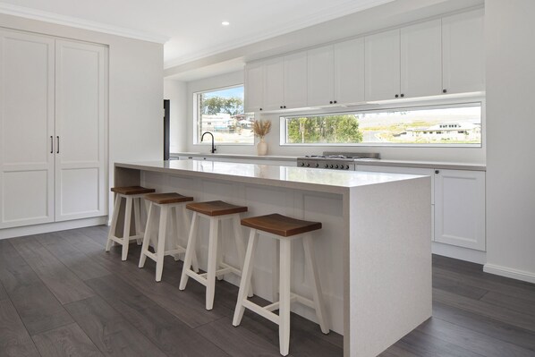 A modern kitchen with a central island, bar stools, and a large window offering a view of the outdoors.