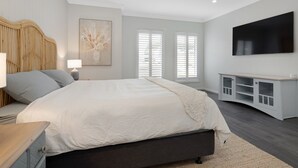Une chambre moderne avec un grand lit, une table de chevet avec une lampe, un téléviseur fixé au mur et une fenêtre avec des stores.