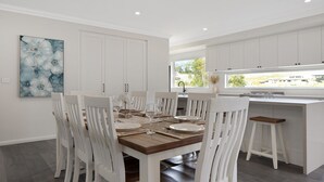 Une cuisine moderne avec des meubles blancs, une table à manger pour six personnes et une grande fenêtre offrant une vue sur l’extérieur.