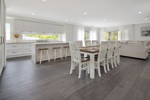 A modern kitchen with white cabinets, a dining area with wooden chairs and a table, and a living area with a sofa.