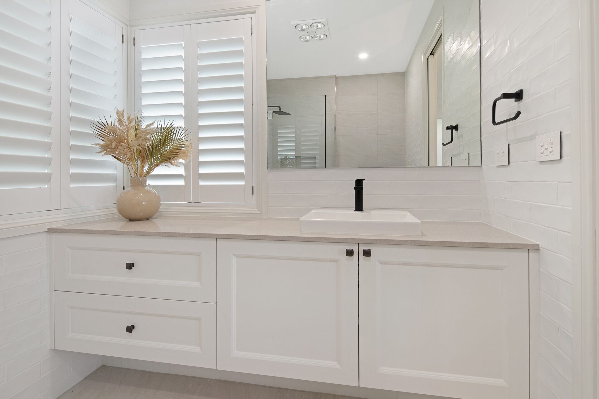A bathroom with white cabinetry, a sink, a mirror, and a window with blinds.