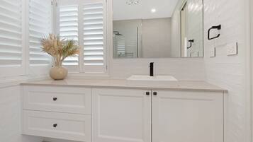 A bathroom with white cabinetry, a sink, a mirror, and a window with blinds.