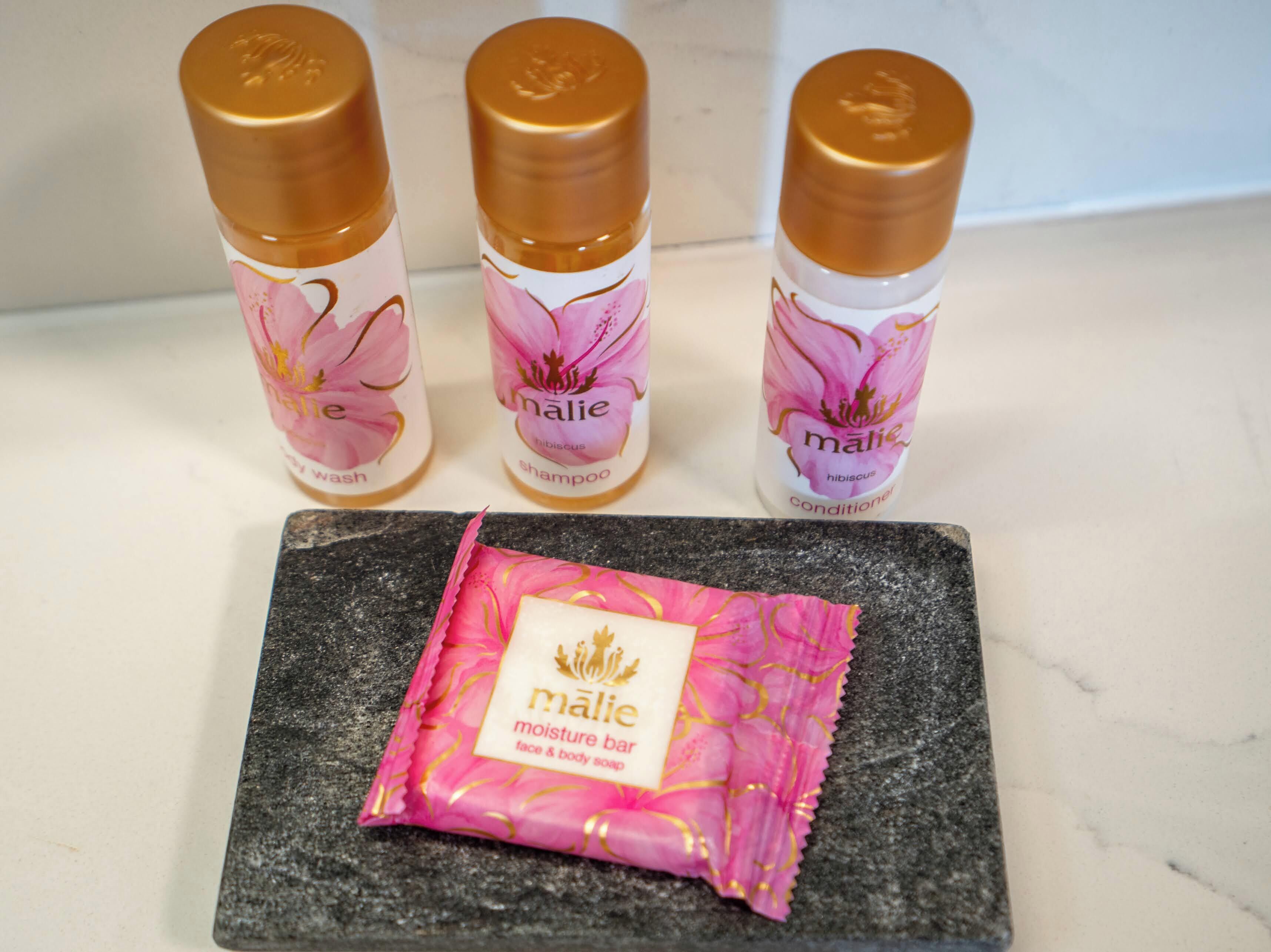 Three bottles of Malie products and a bar of Malie moisture bar soap on a countertop.