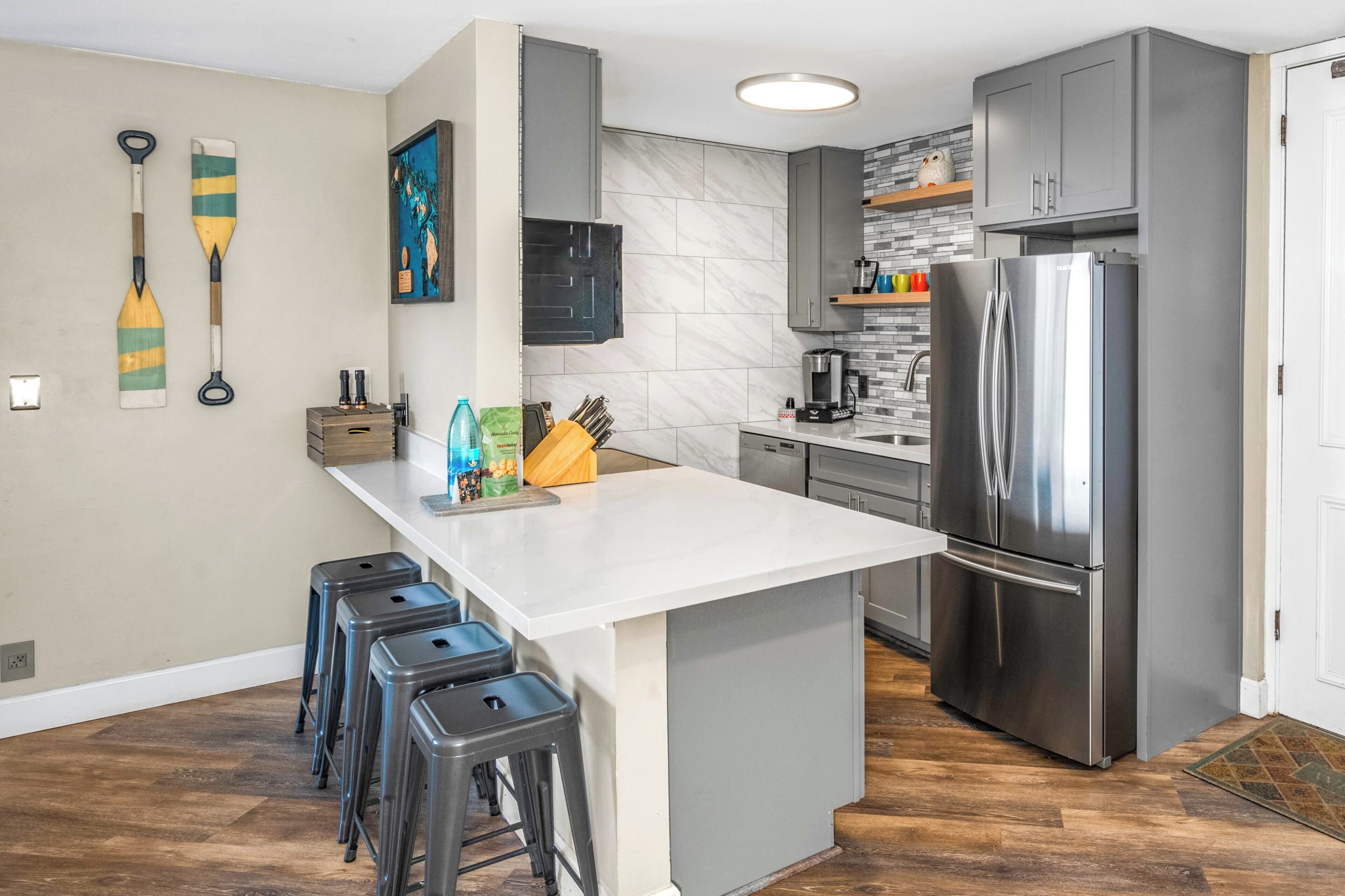 A modern kitchen with a central island, grey cabinets, a stainless steel refrigerator, and a coffee machine.