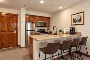 A modern kitchen with granite countertops, stainless steel appliances, and a bar area with stools.
