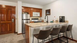 Una cucina moderna con mobili in legno, elettrodomestici in acciaio inossidabile, un piano di lavoro in granito e un angolo bar con sgabelli.