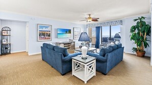 A living room with two blue sofas, a white coffee table, a ceiling fan, and a large window with a view of the city. - $150 activities - E-gift card when you book - Oceanfront | Wrap-Around Balcony | M902 (Myrtle Beach)
