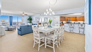 A modern kitchen with white cabinets, a dining area with a glass table, and a living room with a blue sofa. - $150 activities - E-gift card when you book - Oceanfront | Wrap-Around Balcony | M902 (Myrtle Beach)